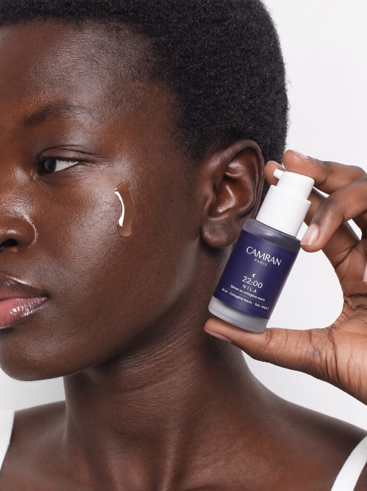Une femme tient un flacon de Sérum Nila près de son visage, une goutte de sérum posée sur la pommette.